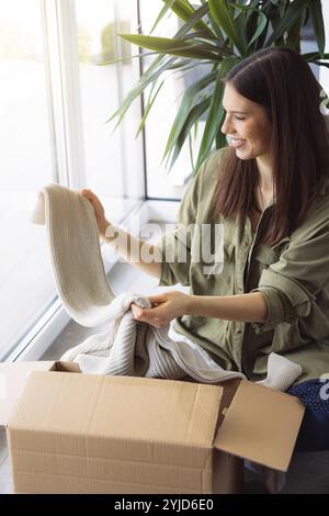 Junge kaukasische Frau erhält eine große Kiste mit ihren Online-Bestellungen. Frau, die das Paket öffnet und begeistert ist, das Zeug zu sehen, das sie gekauft hat. Stockfoto