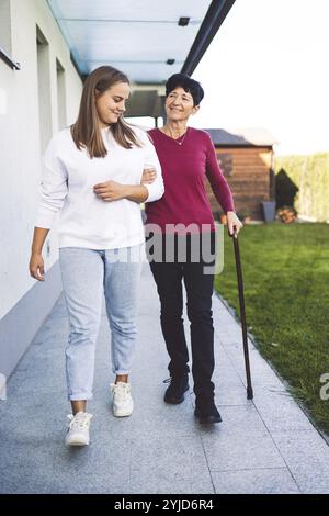 Junge kaukasische Frau, Krankenschwester, bei einem Hausbesuch, um eine Seniorin zu versorgen. Die Schwester hilft einer Seniorin bei den täglichen Aufgaben, hilft ihr, zu laufen Stockfoto