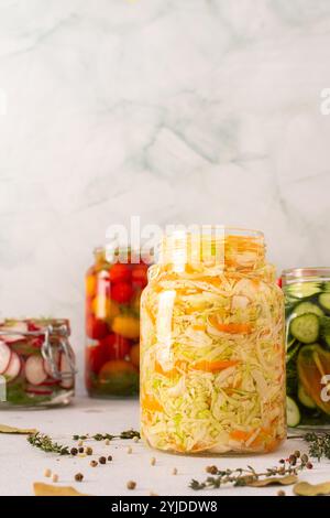 Frischer Weißkohl mit Gärung in einem Glas mit Gewürzen, wodurch ein gesundes probiotisches Essen entsteht, frisches fermentierendes Gemüse wie Radieschen, Tomaten Stockfoto