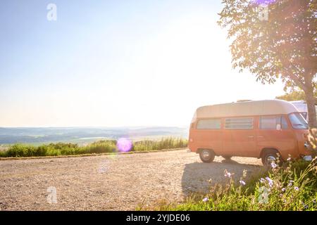 Ein Orange-weisser VW Bus Bulli steht auf einem Schotterparkplatz an einem Sommermorgen, Baden Württemberg, Deutschland. Ein Bulli steht in der Landschaft *** ein orange-weißer VW-Bus steht an einem Sommermorgen auf einem Schotterparkplatz, Baden-Württemberg, Deutschland Ein Van steht in der Landschaft Stockfoto