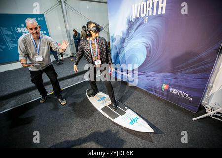 Baku, Aserbaidschan, Aserbaidschan. November 2024. Eine erwachsene Frau versucht, mit einem virtuellen Headset zu surfen, während die Bedienerin sicherstellt, dass sie ausgewogen bleibt. Im Rahmen des portugiesischen Pavillons auf der COP29 wurden im Rahmen der Meeresbewußtseinsbildung die Bildung über Wasser, Meer und auch die unterhaltsamen Aktivitäten interaktiv gemacht. (Kreditbild: © Bianca Otero/ZUMA Press Wire) NUR REDAKTIONELLE VERWENDUNG! Nicht für kommerzielle ZWECKE! Stockfoto