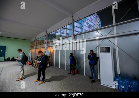 Baku, Aserbaidschan, Aserbaidschan. November 2024. Das beleuchtete Olympiastadion von Baku ist durch ein Fenster zu sehen, während die Gäste ihr Telefon im Inneren eines künstlich geschaffenen Gebäudes betrachten, das für die diesjährige COP29 im Stadion neu eingerichtet wurde. (Kreditbild: © Bianca Otero/ZUMA Press Wire) NUR REDAKTIONELLE VERWENDUNG! Nicht für kommerzielle ZWECKE! Stockfoto