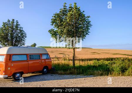 Ein Orange-weisser VW Bus Bulli steht auf einem Schotterparkplatz an einem Sommermorgen, Baden Württemberg, Deutschland. Ein Bulli steht in der Landschaft *** ein orange-weißer VW-Bus steht an einem Sommermorgen auf einem Schotterparkplatz, Baden-Württemberg, Deutschland Ein Van steht in der Landschaft Stockfoto