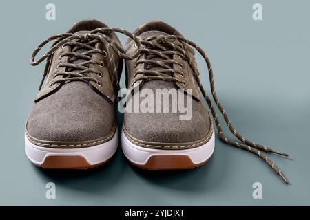 Ein Paar khakifarbene Leinwandschuhe auf silberblauem Hintergrund. Neue braune Sneakers aus Textil mit weißer Sohle in Nahaufnahme. Freizeitschuhe für aktiven Lifestyle. Stockfoto
