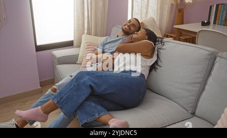 Lächelnder Mann und Frau sitzen zusammen auf einem gemütlichen Sofa in einem modernen Wohnzimmer, um einen liebevollen Moment zu Hause zu genießen. Stockfoto