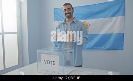 Junger hispanischer Mann, der drinnen mit argentinischer Flagge im Hintergrund an einer Wahlschule wählt Stockfoto