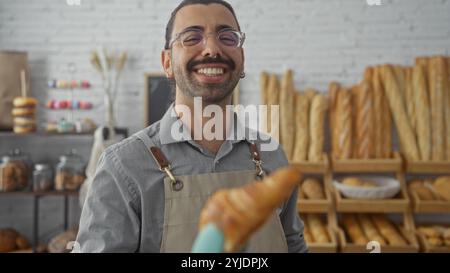 Hispanischer Mann mit einem Schnurrbart, der in einer Bäckerei lächelt und im Hintergrund einen Teig mit Brot- und Gebäckregalen hält. Stockfoto