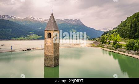 CURON VINSCHGAU, ITALIEN – 27. AUGUST 2024: Aus dem Wasser des Reschensees erhebt sich der berühmte Glockenturm der untergetauchten Vinschgau-Kirche Stockfoto
