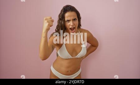 Junge Frau, die heftige Wut in einem Bikini über einem isolierten rosafarbenen Hintergrund ausdrückt Stockfoto