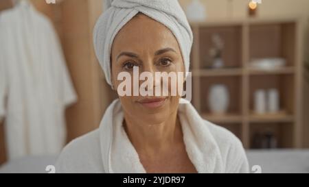 Schöne reife hispanische Frau in einem Spa-Raum mit einem Handtuch um den Kopf gewickelt und genießt eine ruhige Schönheitsbehandlung. Stockfoto