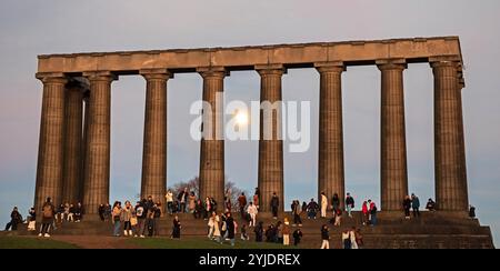 Calton Hill, Edinburgh, Schottland, Großbritannien. November 2024. Touristen treffen sich am malerischen Aussichtspunkt im Stadtzentrum, um den Sonnenuntergang zu beobachten und sie haben den Vollmond als Bonus bekommen. Temperatur leicht 12 Grad Celsius. Im Bild: Touristen schwärmen überall im National Monument und machen Selfies. Mit dem neuen vollen Bibermond im Hintergrund. Hinweis: Am Freitagabend erscheint der supermond. Der volle Beaver Moon steigt am 15. November um 15:30 Uhr GMT in Großbritannien auf und markiert das Ende einer Reihe von vier aufeinanderfolgenden Supermonden. Es werden Live-Nachrichten von Archwhite/Alamy veröffentlicht. Stockfoto