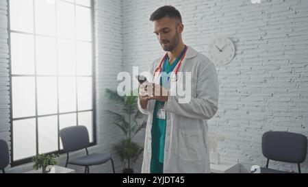 Hispanischer männlicher Arzt mit Bart mit Smartphone im Wartezimmer der Klinik mit modernem Dekor. Stockfoto
