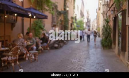 Die Menschen, die auf einer Kopfsteinpflasterstraße in rom spazieren gehen, sind im Bokeh, das das Ambiente eines Cafés im Freien und die historische Architektur einfängt, verschwommen. Stockfoto