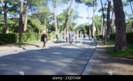Verschwommene Menschen, die in den Gärten der Villa borghese in rom mit üppigen Bäumen und Sonnenschein spazieren, fangen ruhige Atmosphäre im Freien mit defokussiertem Hintergrund und Su ein Stockfoto