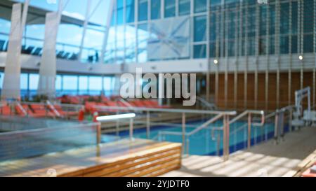 Verschwommenes luxuriöses Kreuzfahrtschiff-Interieur mit Bokeh-Effekt, das den ruhigen Poolbereich und das stilvolle moderne Design mit Sonnenlicht, das durch großen Wind strömt Stockfoto