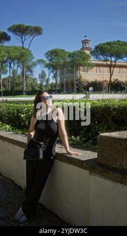 Frau genießt Sonnenlicht in den Gärten der Villa borghese in rom mit lebhaftem Grün und historischer Architektur, die einen ruhigen Moment der Freude und Entspannung einfangen Stockfoto