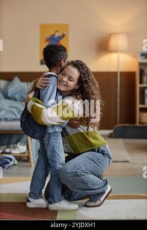 Vertikale Aufnahme einer lächelnden Adoptivmutter, die Schwarzen Jungen sanft umarmt, im Schlafzimmer erzieht ein glückliches, selbstbewusstes Kind, während er den Sohn zur Schule schickt, Kopie s Stockfoto