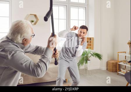 Aggressiver alter männlicher Patient greift jungen Krankenschwester mit Gehstock an und drückt Wut aus Stockfoto