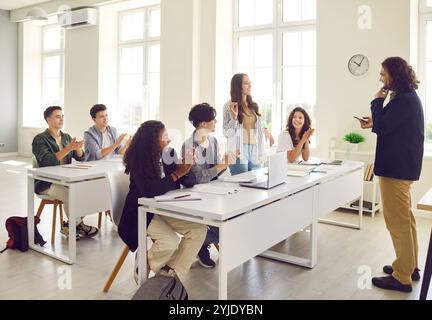 Junge Schülerin, die am Schreibtisch im Klassenzimmer steht und dem männlichen Lehrer antwortet. Stockfoto