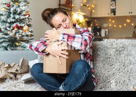 Glückliche junge kaukasische Frau, die zu Hause auf einem Sofa sitzt und ihre Online-Weihnachtsgeschenke annimmt. Stockfoto