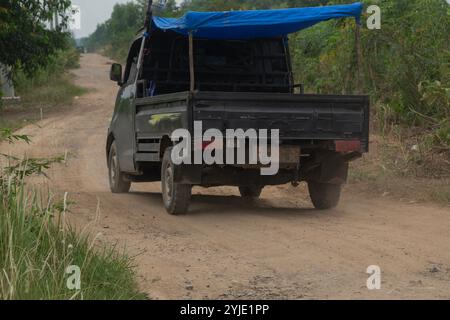 Das Aussehen eines schwarzen Autos auf einer beschädigten Straße mit rotem Staub, einer mit Schlaglöchern versehenen Straße im Landesinneren Indonesiens Stockfoto