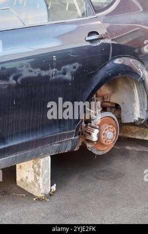 Das Bild zeigt ein Auto mit einem gestohlenen Rad, das zur Unterstützung auf einem Block aufliegt. Diese Szene veranschaulicht die Folgen von Autodiebstahl und dem Chal Stockfoto