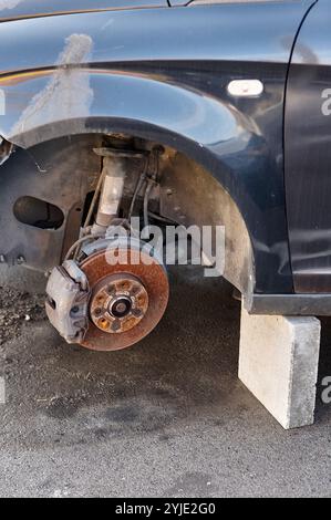 Ein detailliertes Foto eines Fahrzeugs, bei dem ein Rad gestohlen wurde, das von einem Block gestützt wird, um es vom Boden fernzuhalten. Das Bild unterstreicht die Unannehmlichkeiten und Schwachstellen Stockfoto