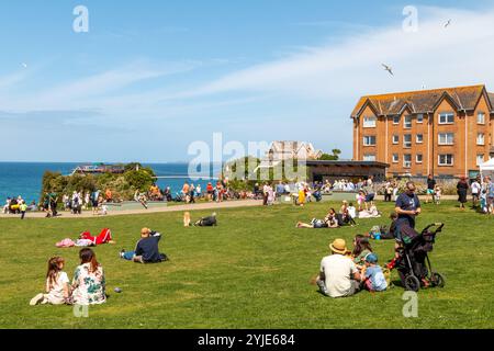 Die Leute sitzen in der Sonne und genießen das gute Wetter und den Meerblick auf Killacourt in Newquay, Cornwall, England, Großbritannien Stockfoto