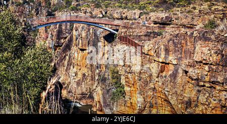 Eine atemberaubende Brücke führt über einen tiefen, felsigen Canyon und zeigt die raue Schönheit der Natur mit lebendigen, strukturierten Klippenformationen. Stockfoto