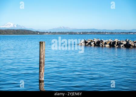 Das blaue Meer, die Berge im Hintergrund und der Wellenbrecher von White Rock, Kanada Stockfoto
