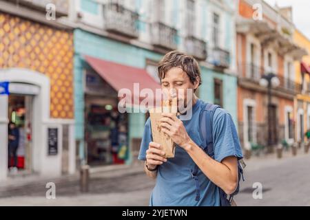 Männlicher Tourist isst Churros auf einer Kolonialstraße in Puebla, Mexiko. Kulturelles Erlebnis, lokale Küche und Streetfood-Konzept Stockfoto