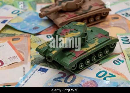 Zwei Spielzeugpanzer, eine Menge Euro-Banknoten. Konzept: staatsausgaben für Armee und Waffen, militärische Hilfe für die Ukraine, tr Stockfoto