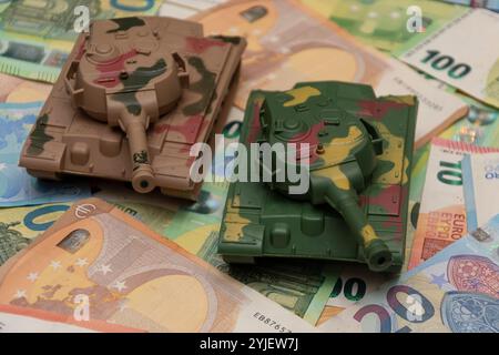 Zwei Spielzeugpanzer, eine Menge Euro-Banknoten. Konzept: staatsausgaben für Armee und Waffen, militärische Hilfe für die Ukraine, tr Stockfoto