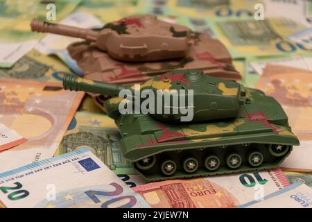 Zwei Spielzeugpanzer, eine Menge Euro-Banknoten. Konzept: staatsausgaben für Armee und Waffen, militärische Hilfe für die Ukraine, tr Stockfoto