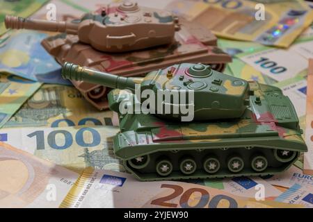 Zwei Spielzeugpanzer, eine Menge Euro-Banknoten. Konzept: staatsausgaben für Armee und Waffen, militärische Hilfe für die Ukraine, tr Stockfoto