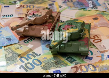 Zwei Spielzeugpanzer, eine Menge Euro-Banknoten. Konzept: staatsausgaben für Armee und Waffen, militärische Hilfe für die Ukraine, tr Stockfoto