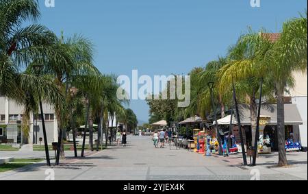 Touristen, die an einem sonnigen Sommertag die von Palmen gesäumte Straße in griechenland entlang laufen Stockfoto