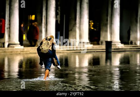 Ein Mann, der eine Frau im Hochwasser in San Marco, Venedig, Italien, unterstützt Stockfoto