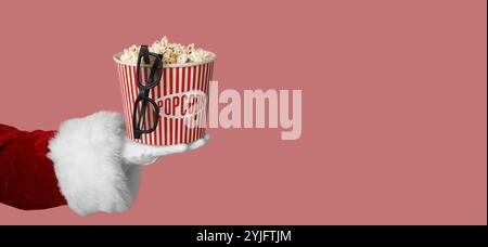 Weihnachtsmann hält einen Eimer mit Popcorn und 3D-Brille auf rosa Hintergrund mit Platz für Text Stockfoto