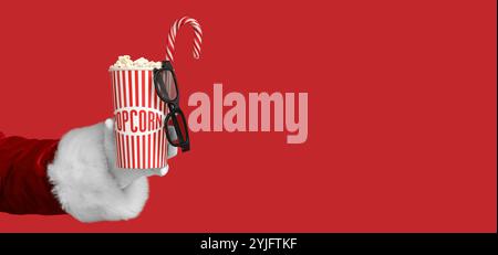 Weihnachtsmann hält einen Eimer mit Popcorn, 3D-Gläser und Zuckerrohr auf rotem Hintergrund mit Platz für Text Stockfoto
