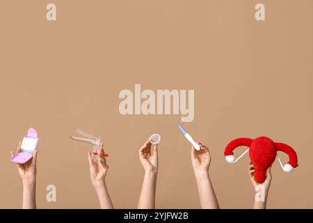 Hände mit weiblichem Uterus, Schwangerschaftstest, Menstruationstasse, Tampons und gynäkologischem Spekulum auf beigem Hintergrund Stockfoto