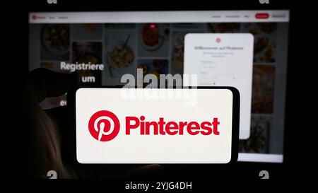 In dieser Abbildung hält eine Person ein Mobiltelefon mit dem Logo des US-amerikanischen Social-Media-Unternehmens Pinterest Inc. Vor der Unternehmenswebseite. Stockfoto