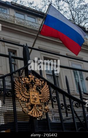 London, Großbritannien. Februar 2018. Die russische Flagge fliegt über dem Adler an den Toren der russischen Botschaft, während Demonstranten auf der anderen Straßenseite Russland Kriegsverbrechen in Syrien vorwerfen und ihnen sagen, das Land zu verlassen. Der von der syrischen Solidaritätskampagne organisierte Protest kam nach einigen der größten Massaker seit dem Chemikalienangriff im vergangenen April, bei dem Frauen und Kinder in Idlib getötet wurden, wo es weiterhin weit verbreitete chemische Angriffe und Bombardements gegen Krankenhäuser und medizinische Teams gab. Der jüngste Anstieg von Angriffen folgt dem Abschuss eines russischen Jets über Idlib durch syrische Freiheitskämpfe Stockfoto