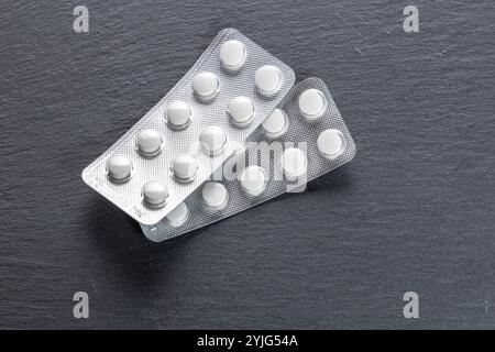 Zwei Blisterpackungen mit weißen Tabletten, eine übereinander, liegen auf einer schwarzen Schieferoberfläche. Stockfoto