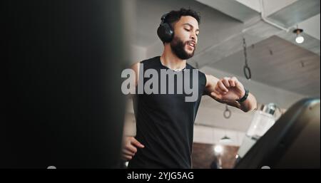 Mann, trainieren und überprüfen Sie auf dem Laufband im Fitnessstudio die Laufgeschwindigkeit, überwachen Sie die Leistung und das Cardio-Training. Kopfhörer, Maschine oder Person, die zuhört Stockfoto