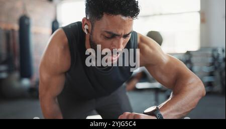 Mann, trainieren und überprüfen Sie die Uhr im Fitnessstudio auf Herz-Kreislauf-Geschwindigkeit, überwachen Sie Leistung und Ausdauertraining. Kopfhörer, Fahrradgerät und Hörer Stockfoto