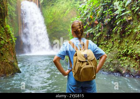 Weibliche Touristenin mit Rucksack, die den Blick auf den fantastischen Wasserfall genießt Stockfoto