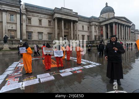 London, Großbritannien. Januar 2018. Auf einem Platz am Trafalgar Square stehen Demonstranten in orangefarbenen Anzügen und schwarzen Kapuzen, die 16 Jahre des illegalen Gefangenenlagers in Guantanamo Bay markieren. Die Namen der 41 verbliebenen Häftlinge wurden vorgelesen, von denen viele auf unbestimmte Zeit ohne Anklage oder Gerichtsverfahren festgehalten wurden, fast alle, die von afghanischen Milizen und dem pakistanischen Militär gegen Geldgelder an die USA verkauft wurden, ohne dass es tatsächlich Beweise für eine terroristische Beteiligung gab, deren Folter aber in geheimen CIA-Gefängnissen auf der ganzen Welt vor der Ankunft in Guantanamo ebenso wie während ihrer gesamten Inhaftung auch ihre Freilassung gibt Stockfoto