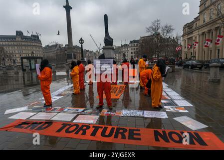 London, Großbritannien. Januar 2018. Auf einem Platz am Trafalgar Square stehen Demonstranten in orangefarbenen Anzügen und schwarzen Kapuzen, die 16 Jahre des illegalen Gefangenenlagers in Guantanamo Bay markieren. Die Namen der 41 verbliebenen Häftlinge wurden vorgelesen, von denen viele auf unbestimmte Zeit ohne Anklage oder Gerichtsverfahren festgehalten wurden, fast alle, die von afghanischen Milizen und dem pakistanischen Militär gegen Geldgelder an die USA verkauft wurden, ohne dass es tatsächlich Beweise für eine terroristische Beteiligung gab, deren Folter aber in geheimen CIA-Gefängnissen auf der ganzen Welt vor der Ankunft in Guantanamo ebenso wie während ihrer gesamten Inhaftung auch ihre Freilassung gibt Stockfoto