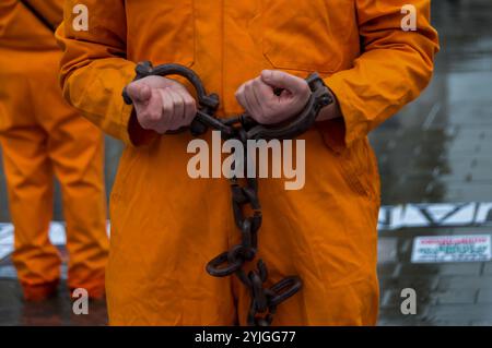 London, Großbritannien. Januar 2018. Auf einem Platz am Trafalgar Square stehen Demonstranten in orangefarbenen Anzügen und schwarzen Kapuzen, die 16 Jahre des illegalen Gefangenenlagers in Guantanamo Bay markieren. Die Namen der 41 verbliebenen Häftlinge wurden vorgelesen, von denen viele auf unbestimmte Zeit ohne Anklage oder Gerichtsverfahren festgehalten wurden, fast alle, die von afghanischen Milizen und dem pakistanischen Militär gegen Geldgelder an die USA verkauft wurden, ohne dass es tatsächlich Beweise für eine terroristische Beteiligung gab, deren Folter aber in geheimen CIA-Gefängnissen auf der ganzen Welt vor der Ankunft in Guantanamo ebenso wie während ihrer gesamten Inhaftung auch ihre Freilassung gibt Stockfoto